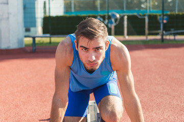 Focused young professional male Caucasian athlete ready for the run race in a sprint starting...