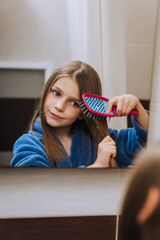Red-haired beautiful teenager girl, child combs her hair, taking care of herself, looking in the...