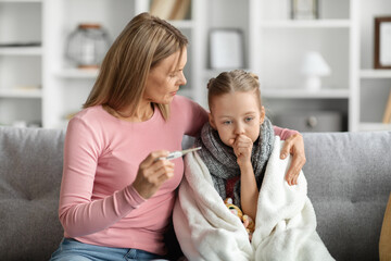 Flu Concept. Worried mother checking her daughter's temperature at home