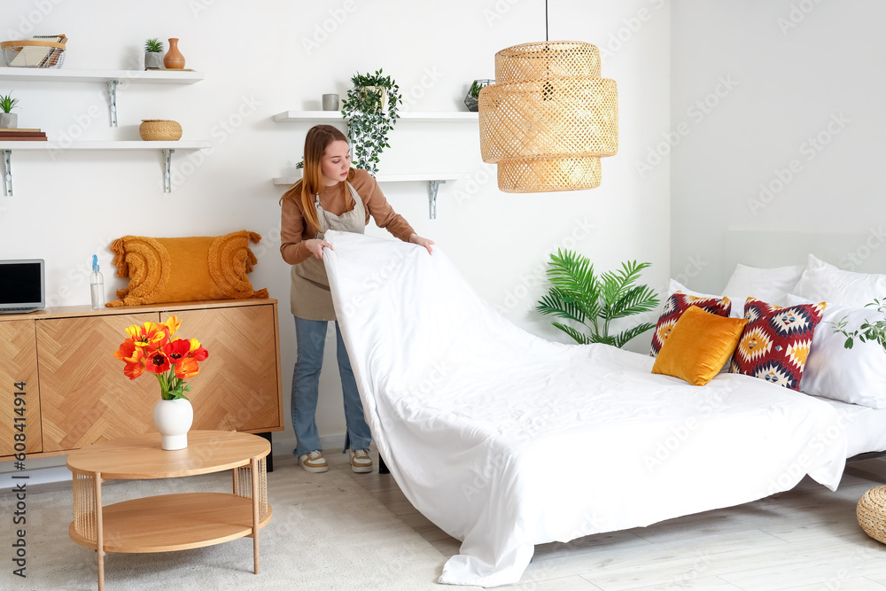 Poster Young woman making bed in bedroom