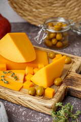 Board with tasty cheddar cheese, olives and thyme on grunge background, closeup