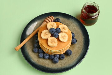 Plate with sweet pancakes, banana, blueberry and honey on green background