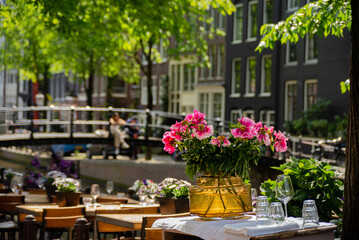 Fototapeta na wymiar Charming restaurant table with glasses and flowers near the canal, streets of Amsterdam,