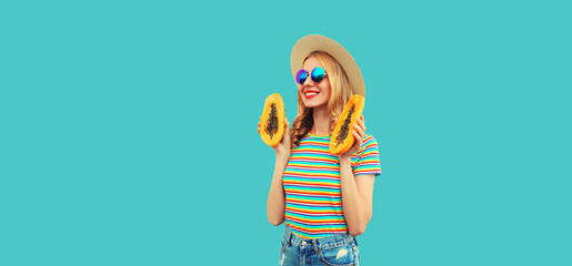 Summer portrait of happy cheerful young woman having fun with fresh papaya fruits wearing straw hat, sunglasses on blue background
