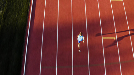 Caucasian male sprint runner alone on the athletic track, taking starting position and running in line four, aerial above shot.