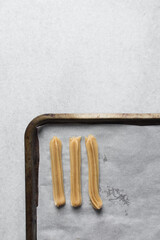Churros dough piped on a parchment lined baking sheet, choux pastry dough about to be fried, process of making churros