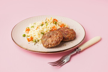 Cutlets with bulgur, boiled vegetables and fork on pink background