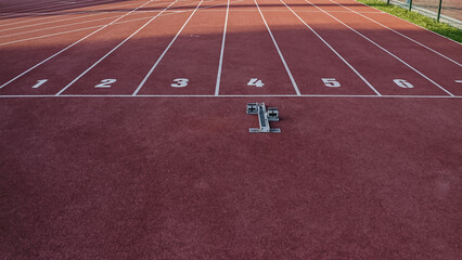 Starting block and starting line of the red tartan athletic track with eight lanes, drone shot.