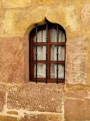 A beautiful antique window made of modern materials in a stone wall of an old restored house protected by figured decorativel bars