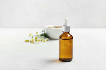 Bottle of essential oil, dried and fresh chamomile flowers on light background