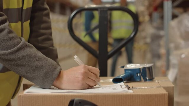 Midsection of unrecognizable warehouse worker using adhesive tape dispenser to pack cardboard box and signing invoice paper, preparing parcel for transportation and dispatching