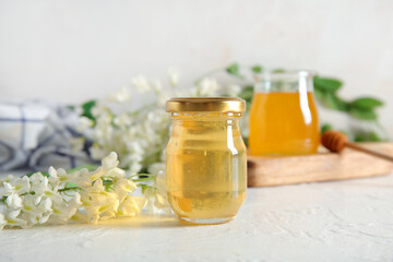 Jars of honey with flowers of acacia on light background, closeup
