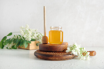 Fototapeta na wymiar Jar of honey with flowers of acacia and dipper on light background