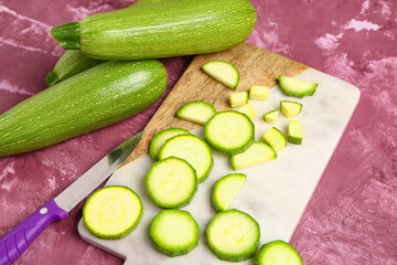 Fresh green zucchini and board with slices on purple background