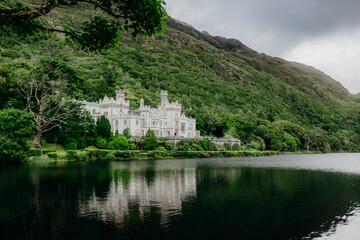 Fototapeta na wymiar Kylemore Abbey castle in Ireland with water in foreground and castle on left side of frame. Wide photo from across water.