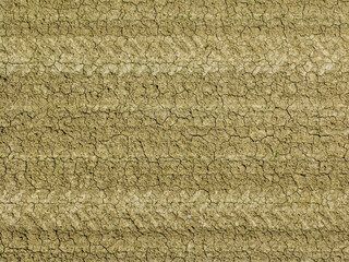 Aerial view of dry earth field with tractor tire tracks in soil with cracks.