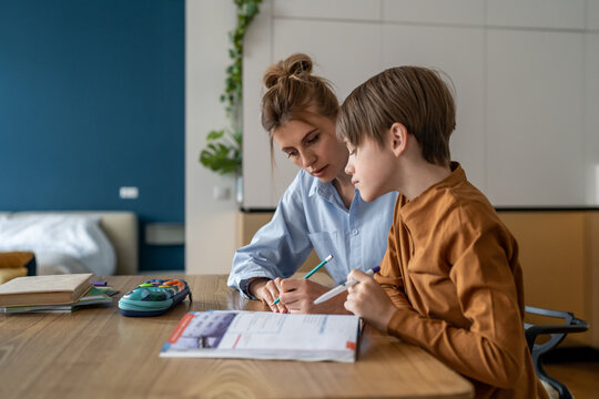 Schoolboy studying with mom, having lesson with private teacher at home, tutor sitting at kitchen table with little boy child explaining exercise, teaching kids foreign language. Homeschooling concept