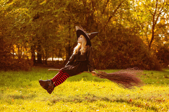 A girl in a witch costume sits on a floating broom
