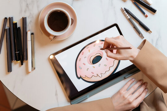 Overhead view of an Illustrator sitting at a table drawing a donut on a digital tablet