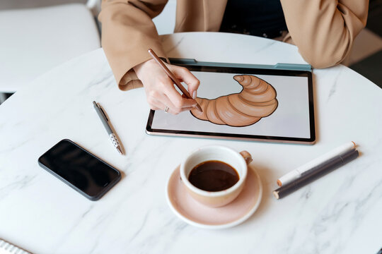 Overhead view of an Illustrator drawing a croissant on a digital tablet