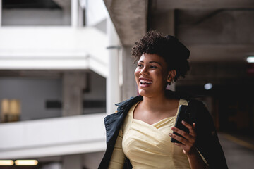 close-up portrait of a smiling afrodescendant latina woman with curly hair looking to the side with cell phone in her hand