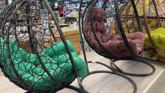 Swinging cocoon chairs made of plastic weaving and colorful mattresses for them. Garden swing chair made of rattan vines in the store. concept of relaxation with a hammock