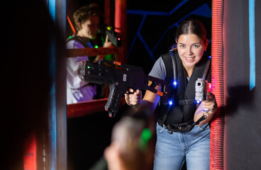 Fototapeta na wymiar Smiling girl with laser pistol during playing laser tag with her friends in dark room