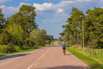 Woman on bicycle on countryside road on bright summer day. Sweden.