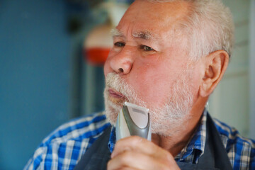 An elderly man trims his beard with an eclectic razor. ease of use of clippers.