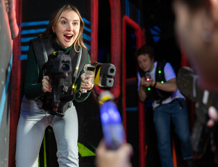 Positive girl holding laser pistol playing laser tag game with his friends