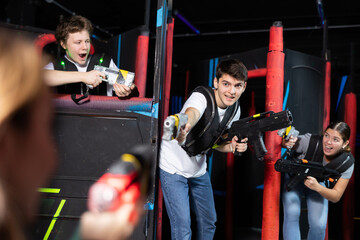 Laughing players young mens and womens playing in teams in dark laser tag station