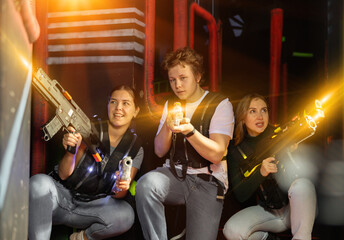 Fototapeta na wymiar Modern satisfied young people with laser pistols playing laser tag on dark labyrinth