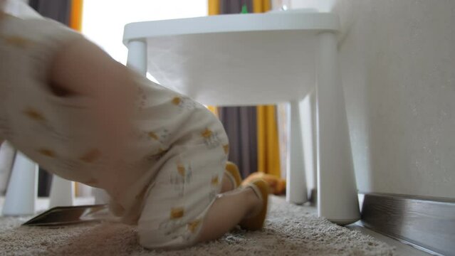 Baby boy crawls under the desk. Happy little kid having fun time at home. Low angle view.