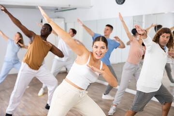 Joyful flexible multiethnic men and women exercising active moves with group of people in dance center