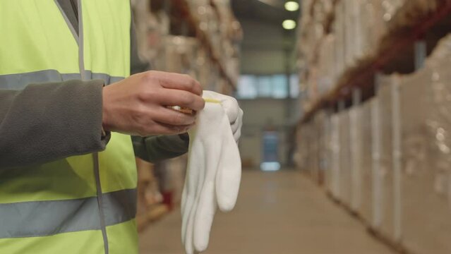 Midsection of unrecognizable warehouse worker putting on disposable gloves preparing for loading and unloading of goods in cardboard boxes