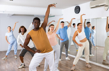 Fototapeta na wymiar African-american man practicing active dance moves during rehearsal with group in dancing studio.