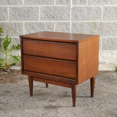 Two-drawer wooden nightstand. Mid-century modern furniture. Product photograph in front of an exterior wall.