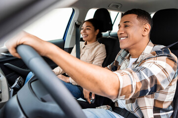 Happy multiracial man and woman going on summer vacation by car, diverse couple sitting inside their new auto, cheerfully smiling looking at road - Powered by Adobe
