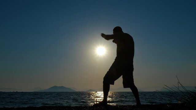 Man silhouette boxing on coast. Active man silhouette practising boxing on the beach during nightfall in summer. A concept of sport in men's life for health.