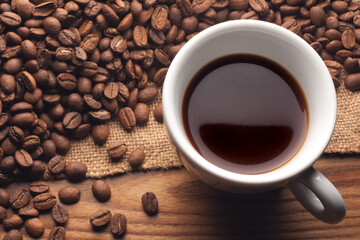 Cup black coffee. Roasted beans on sack on wooden table.