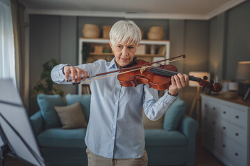 Mature senior caucasian woman learn to play violin practice at home
