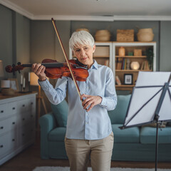 Mature senior caucasian woman learn to play violin practice at home