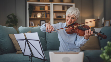 Mature senior caucasian woman learn to play violin practice at home