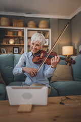 Mature senior caucasian woman learn to play violin practice at home