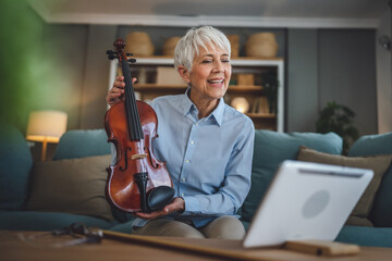 Mature senior caucasian woman learn to play violin practice at home