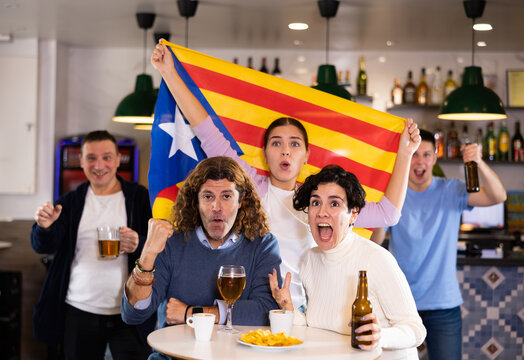Company of emotional young adult fans supporting favorite team of Estelada with flag while resting in sports bar