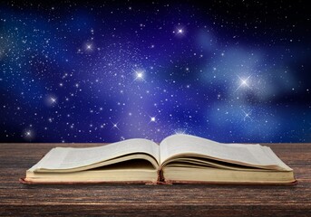 Open antique old book on table with night sky