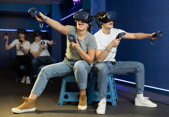 In interactive entertainment club, guy with girl in VR helmets and with joysticks sit and control movement of heroes of popular multiplayer adventure game