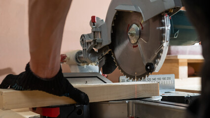 The master cuts the board with a circular saw in the workshop. Close-up of a carpenter's male hands at work.