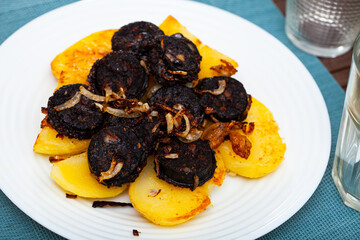 Fried morcilla (blood sausage with rice) served with side dish of baked potatoes